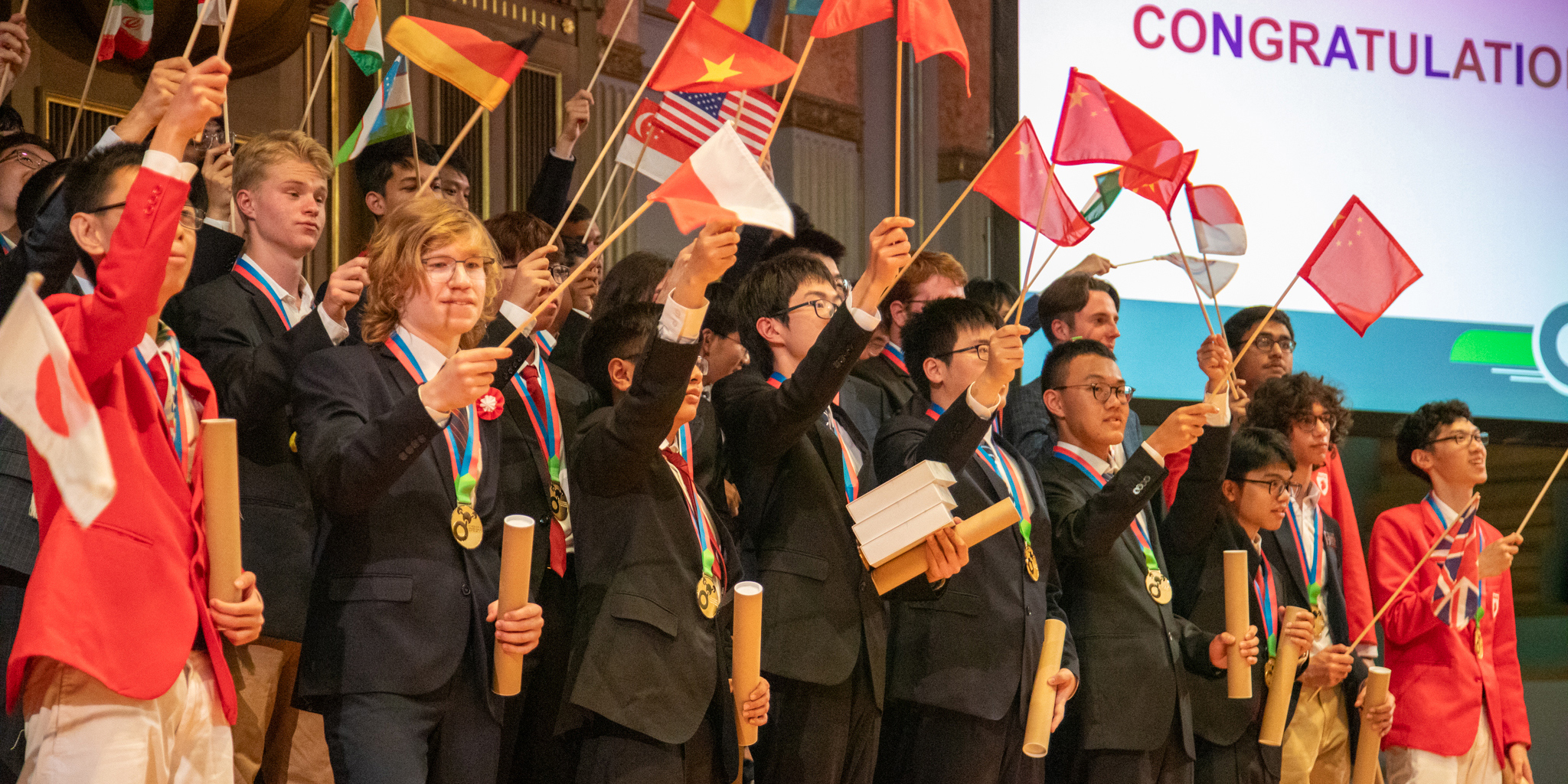 Die Menschen stehen zusammen. Sie halten ein Diplom und die Flagge ihrer eigenen Nation in der Hand. Link zum News Artikel zur Chemie Olympiade.