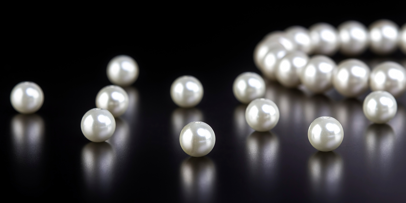 Eine weisse Perlenkette und einzelne Perlen auf einem schwarzen Tisch
