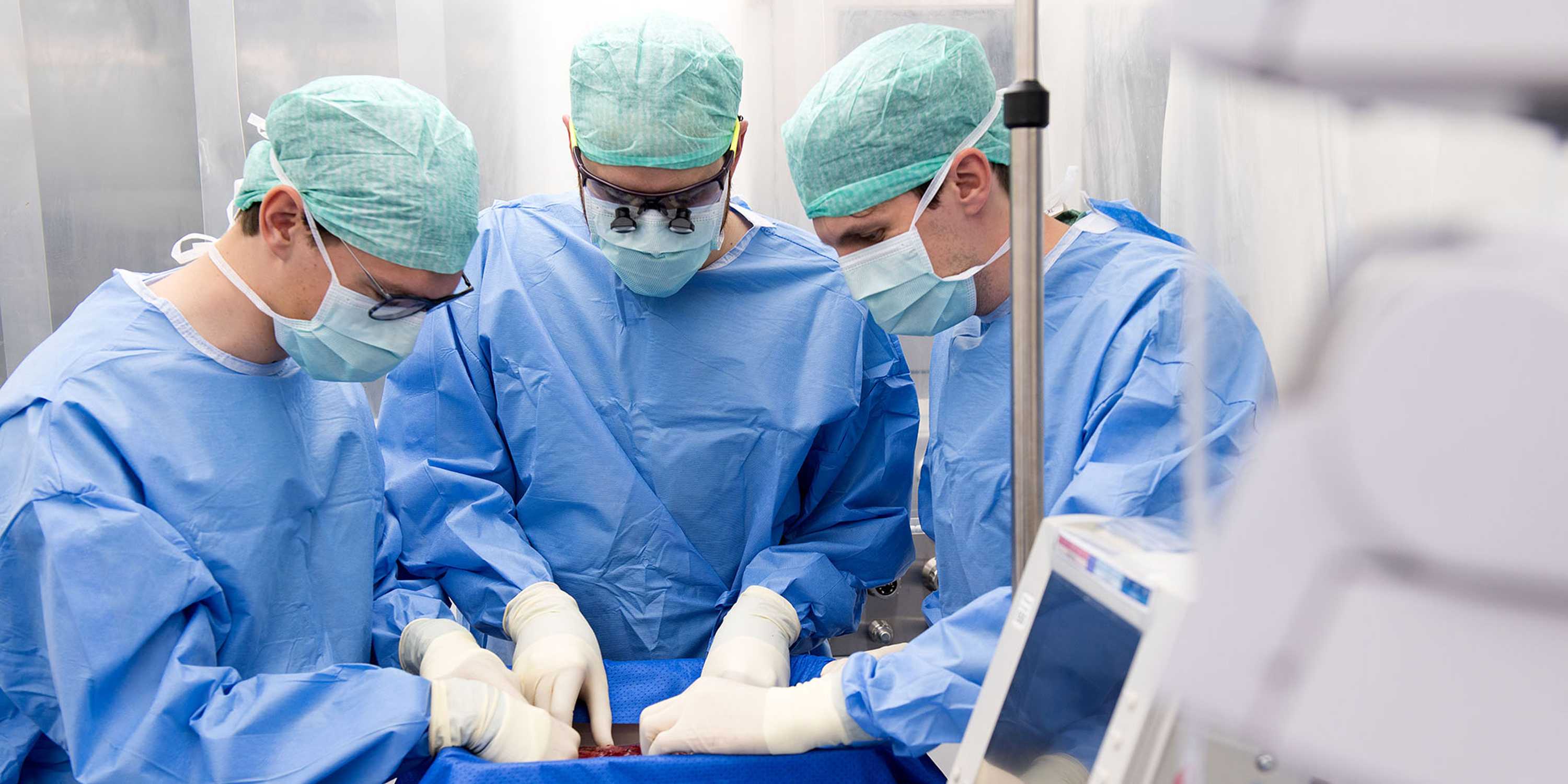 3 Chirurg:innen sind über die Perfusionsmaschine gebeugt