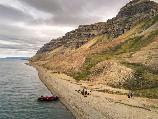 Vergrösserte Ansicht: Schlauchboot und Mensch am Strand, am Rande einer Steilklippe