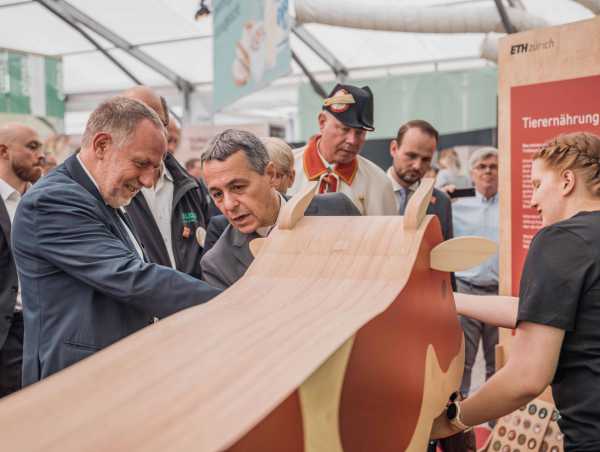 Bundespräsident Ignazio Cassis (in der Bildmitte) steht zusammen mit Detlef Günther (links) hinter einer Holzkuh.