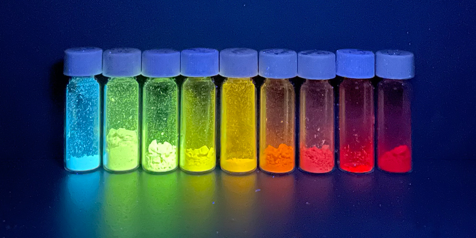 Kleine Gläschen mit fluoreszierenden Substanzen. Diese leuchten in Regenbogenfarben.