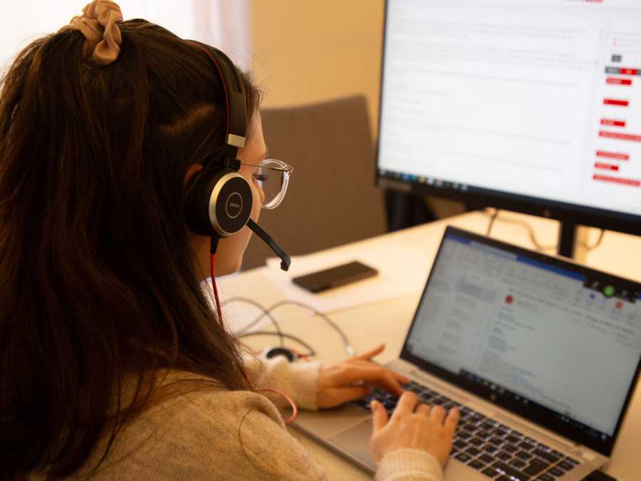 Schriftdolmetscherin beim Tippen auf einem Laptop. Vor ihr ein Zweitbildschirm mit abgebildeter Chatfunktion für das Schriftdolmetschen.