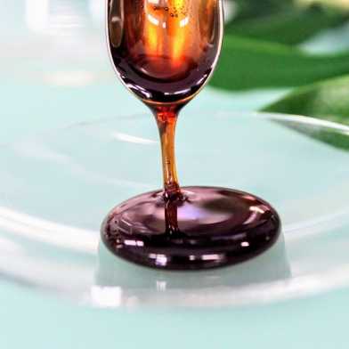 Substanz, die wie dunkler Honig aussieht, läuft von Löffel auf Glasschale. 