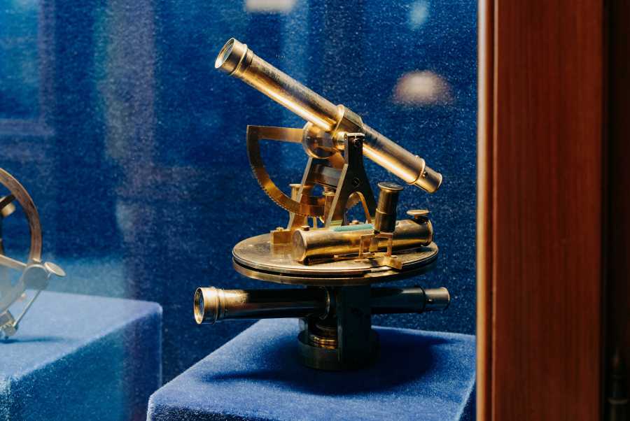 Vergrösserte Ansicht: Blick in eine Vitrine, in welcher vor blauem Hintergrund ein goldenes Winkelmessgerät ausgestellt ist.