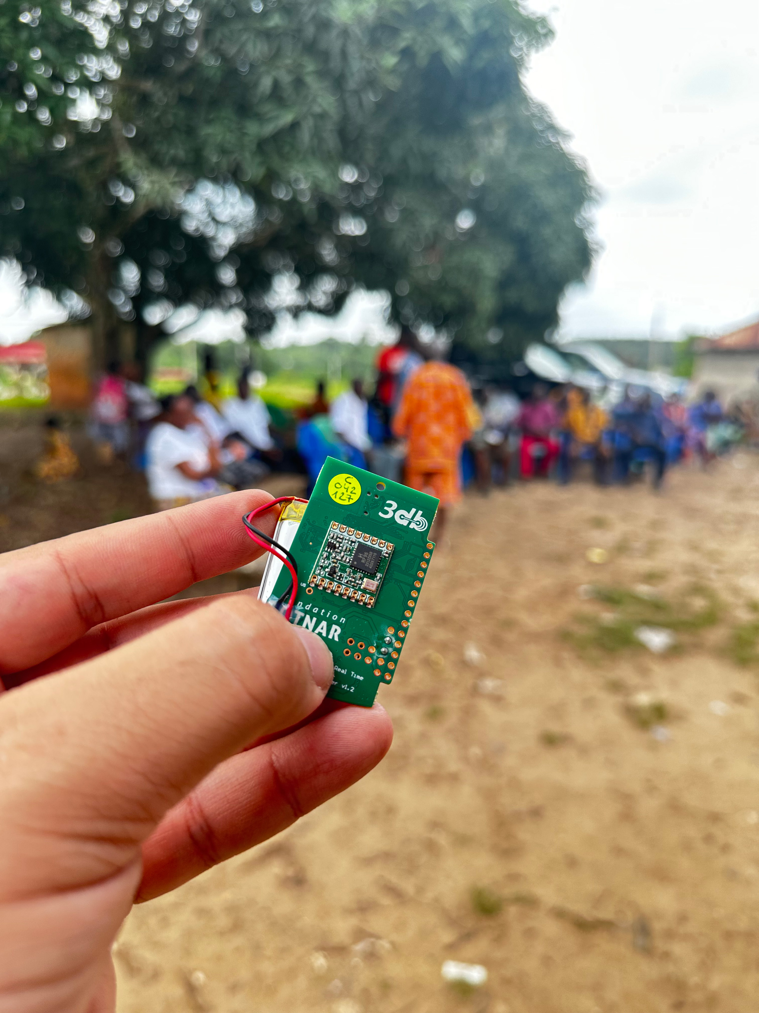 Vergrösserte Ansicht: Hand welche den kleinen grünen Sensor hält, im Hintergrund ist ein afrikanisches Dorf erkennbar.