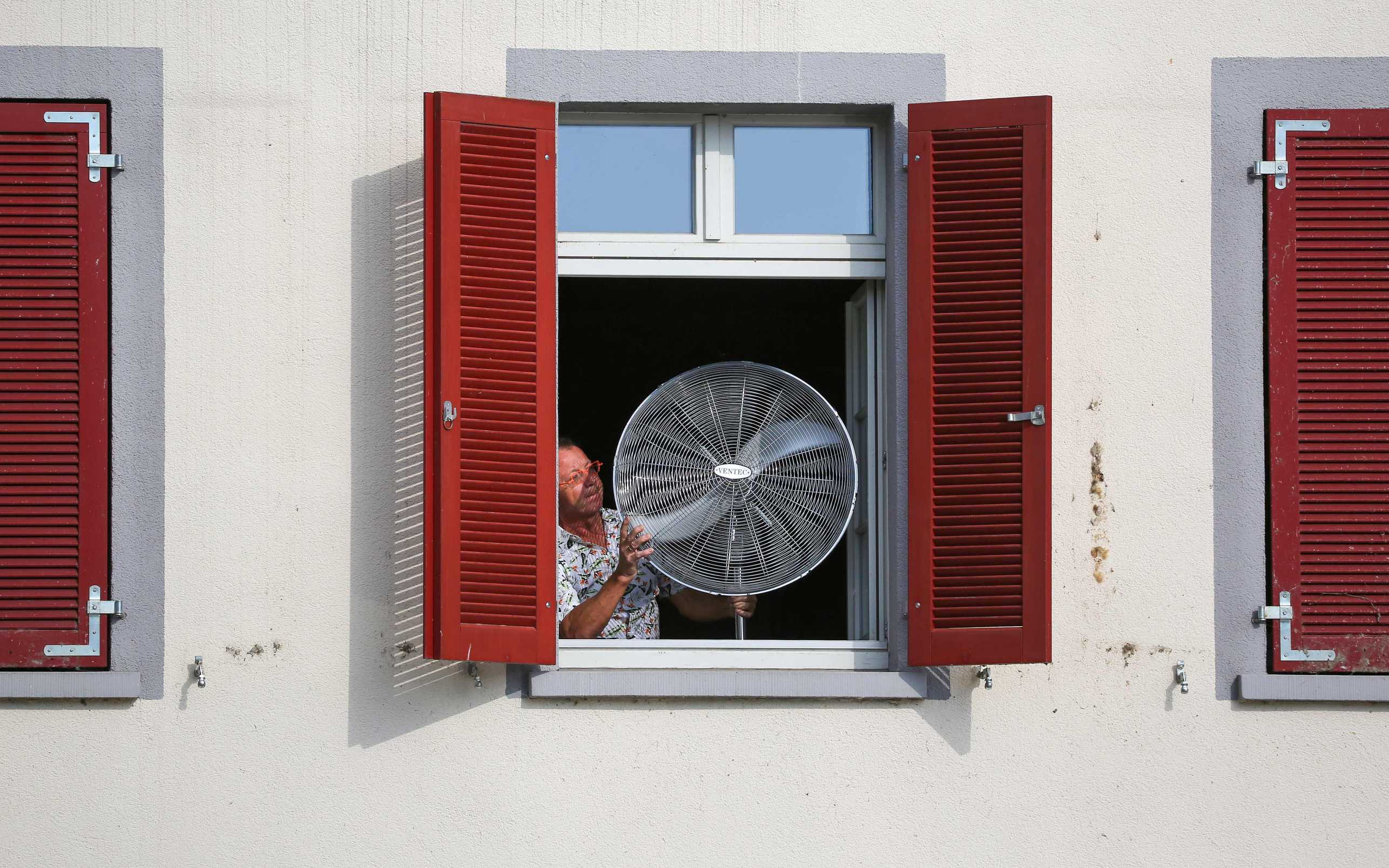 Mann mit einem Ventilator am Fenster