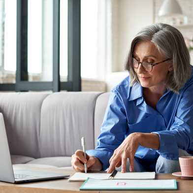 Frau sitzt auf dem Sofa und arbeitet am Laptop