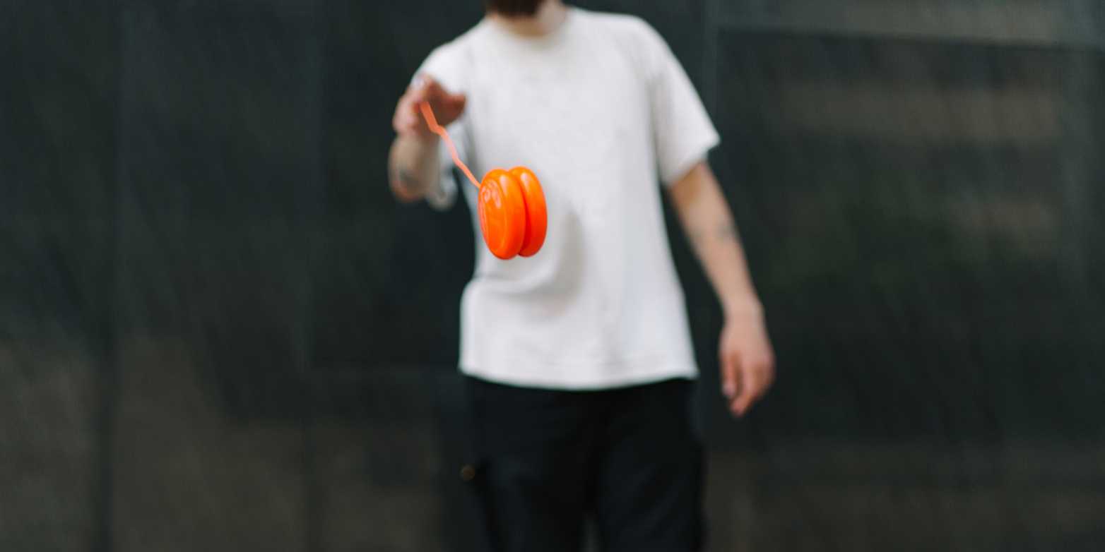 Eine person im Hintergrund schwingt ein orangenes Jojo, welches im Fokus liegt