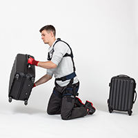 Mann trägt Exoskelett und hebt schweren Koffer