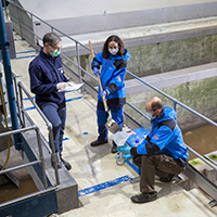 three researchers taking samples at sewage treatment plant.