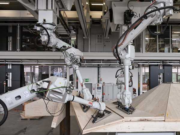 Robotic arms hold wooden panels in a production hall
