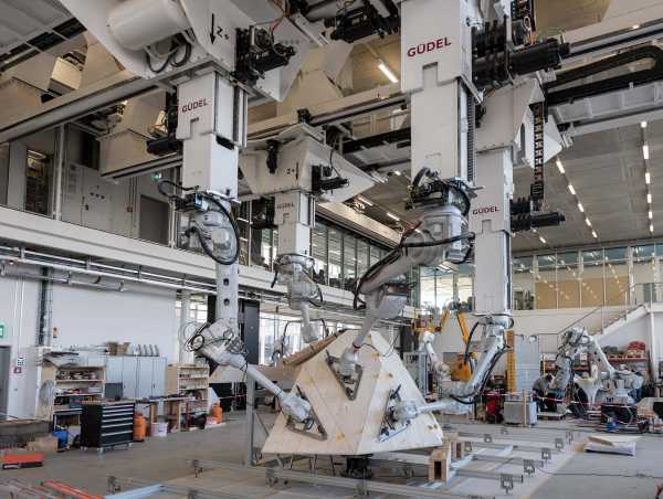 Robotic arms hold wooden panels in a production hall