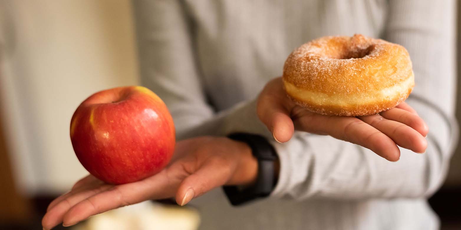 Two hands holding an apple (left) and a doughnut (right)