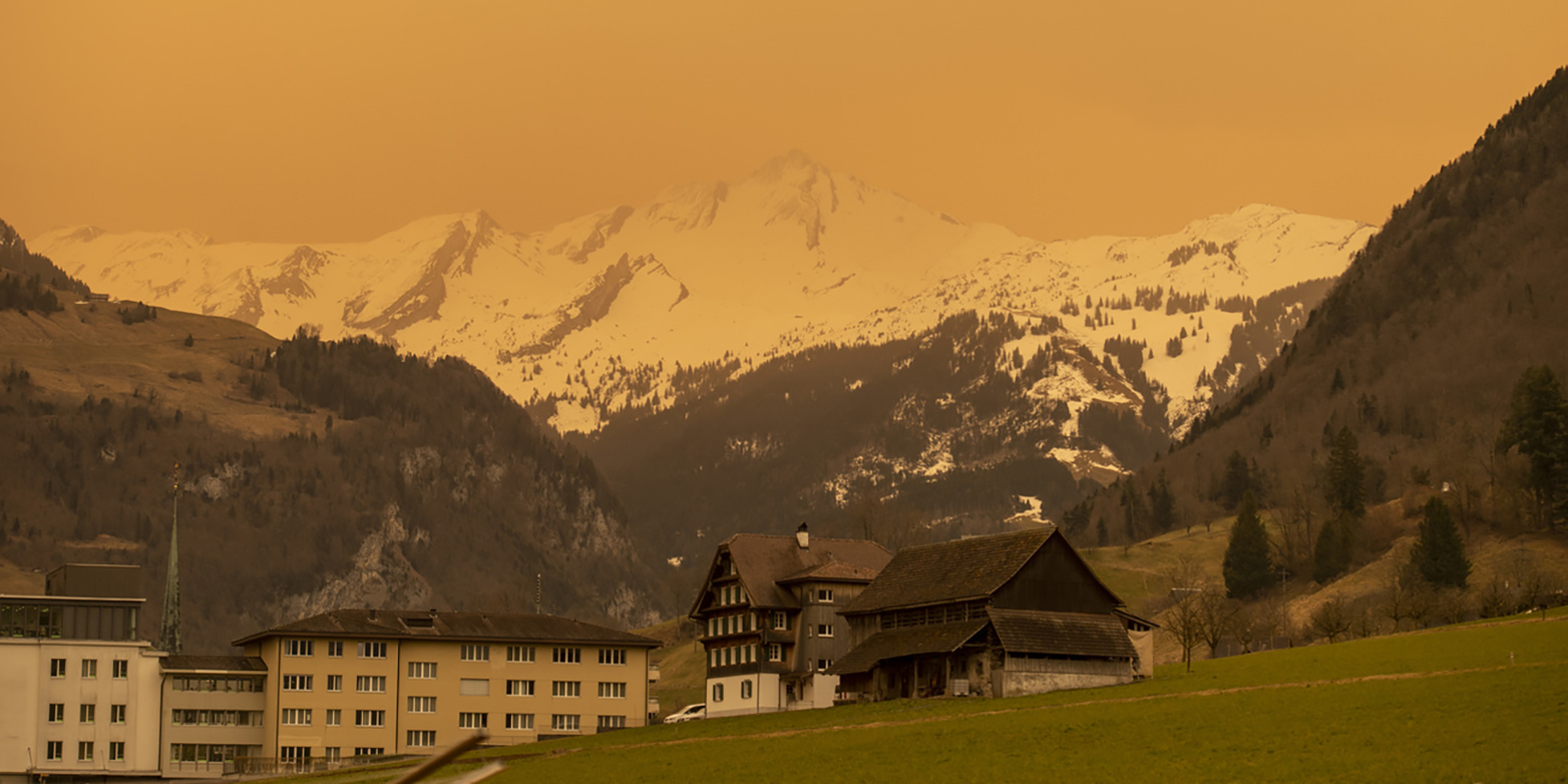 Residential houses with mountain landscape in the background, with everything bathed in orange light.