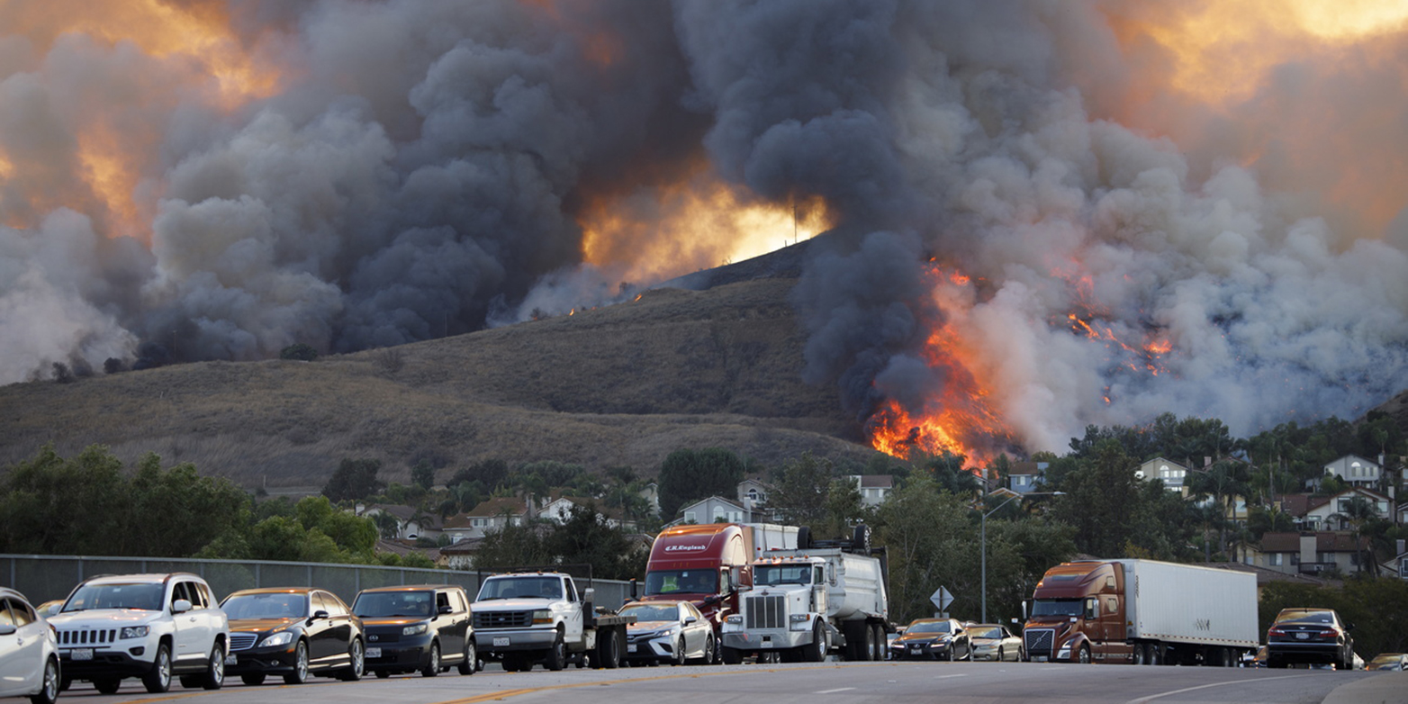 A mountain with a forest fire in the background and cars stuck in a traffic jam in front of it in the foreground 