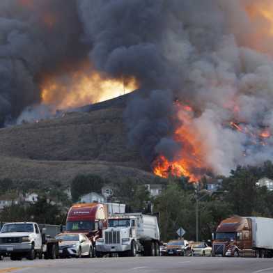 A mountain with a forest fire in the background and cars stuck in a traffic jam in front of it in the foreground 