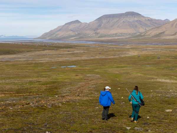 Enlarged view: Two women walking across the tundra, mountains and sea in the background