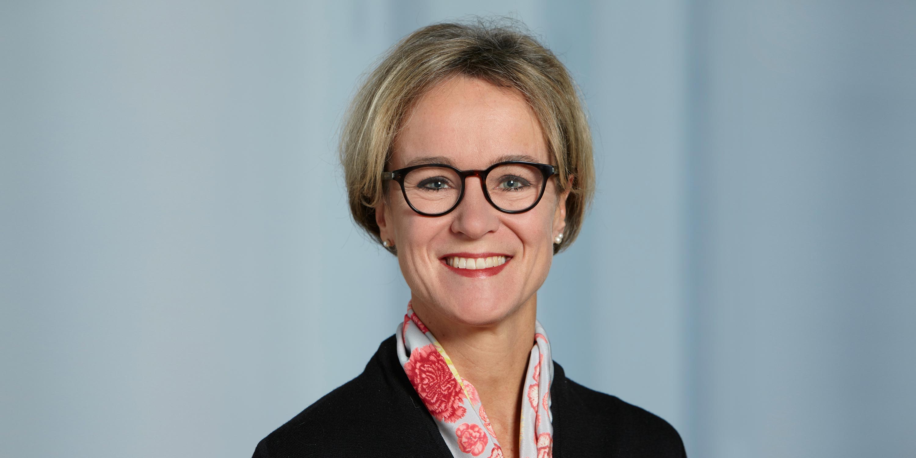 Portrait photo of Annette Oxenius with glasses and scarf, laughing.