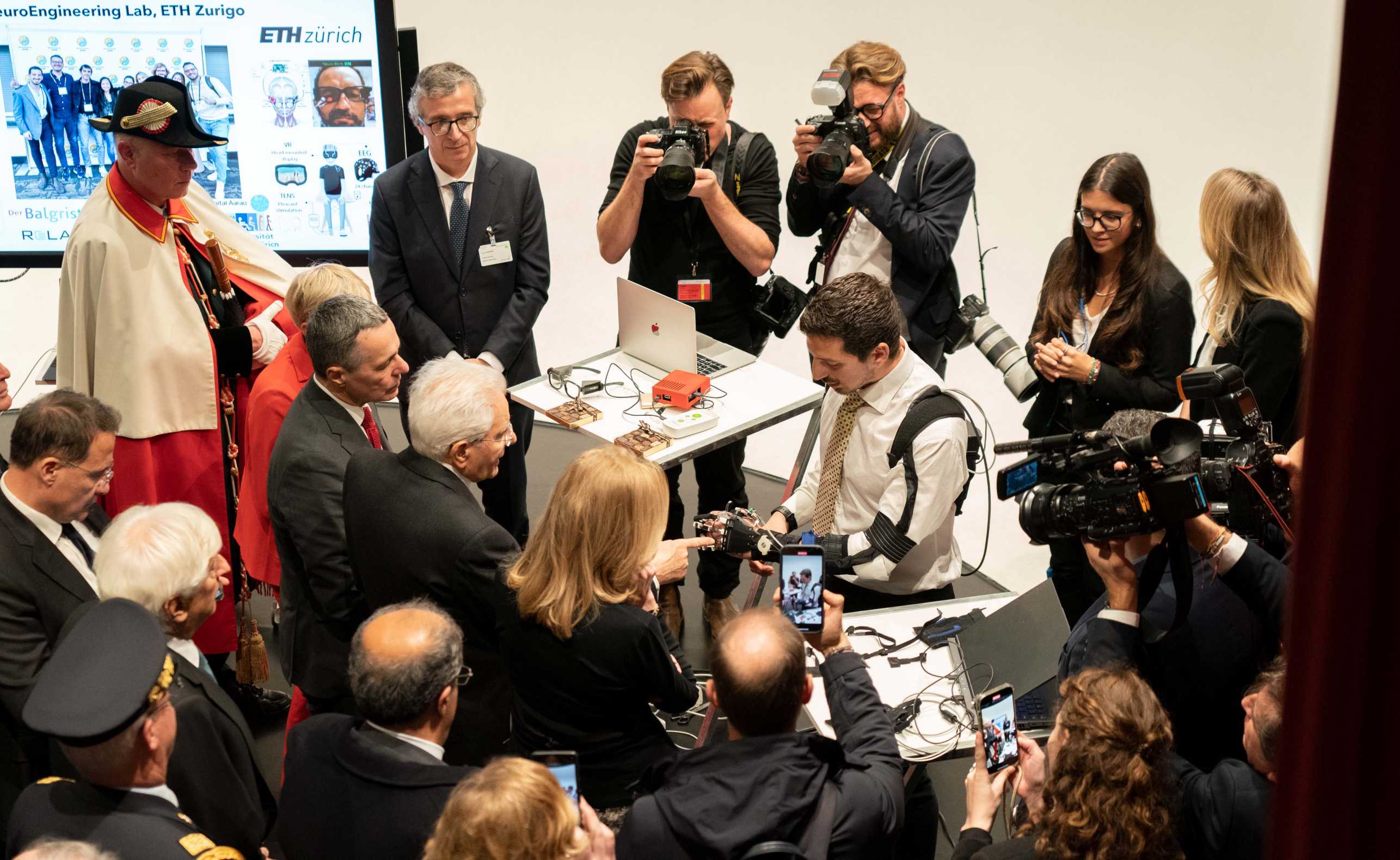 Group of people gathered around a man in a white shirt looking at a robot.