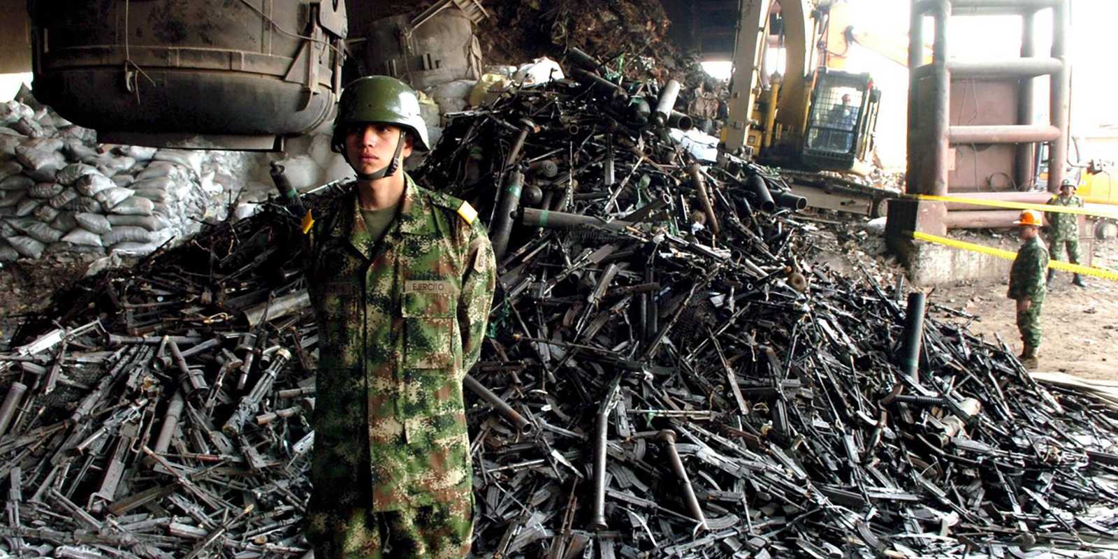 On the left there is a soldier in uniform. Behind him there is a pile of weapons.