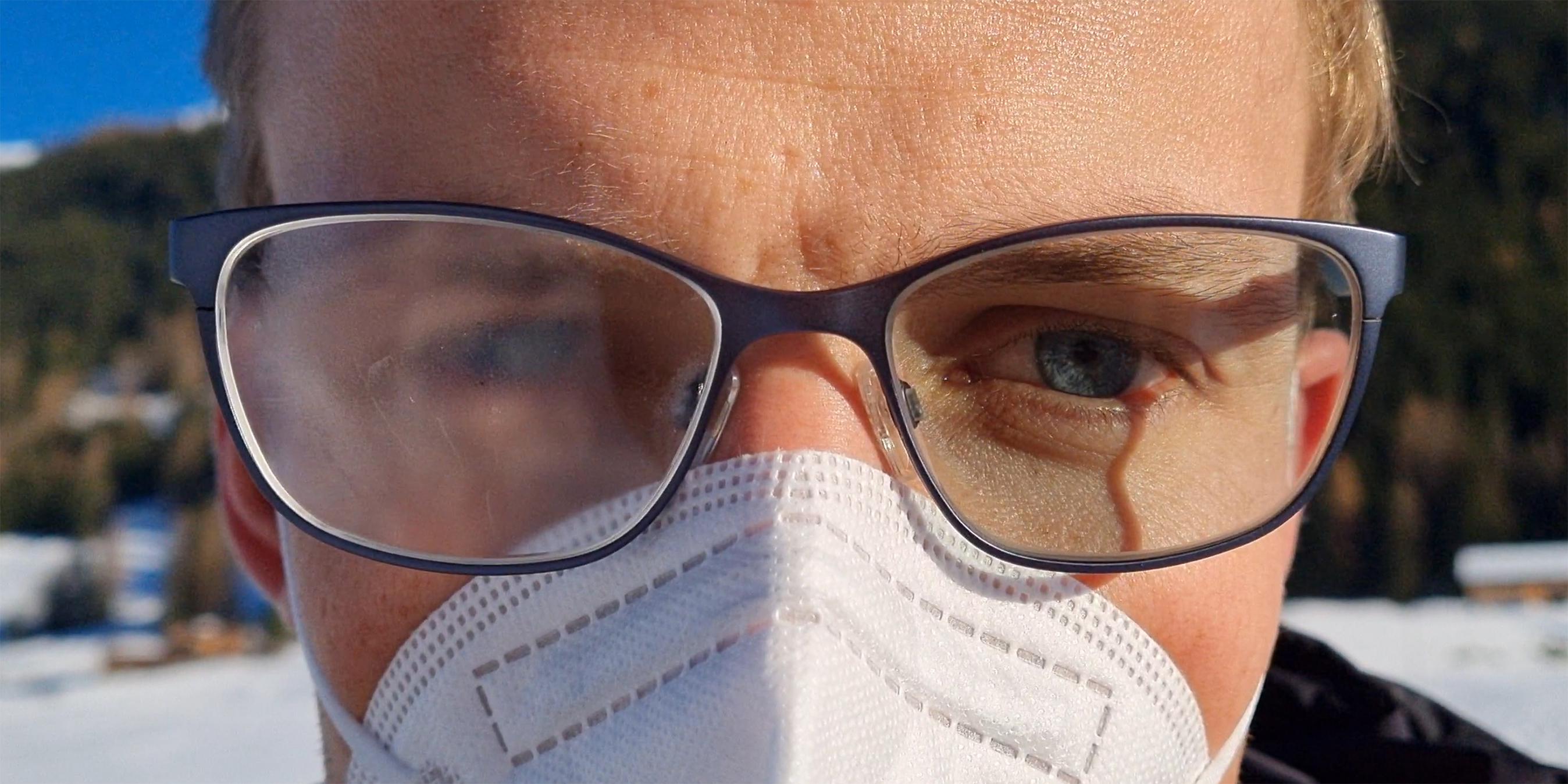 Close-up of man's face. He's wearing a FFP2 mask and glasses in winter. His right eyeglass lens is fogged up.