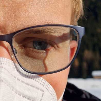 Close-up of man's face. He's wearing a FFP2 mask and glasses in winter. His right eyeglass lens is fogged up.