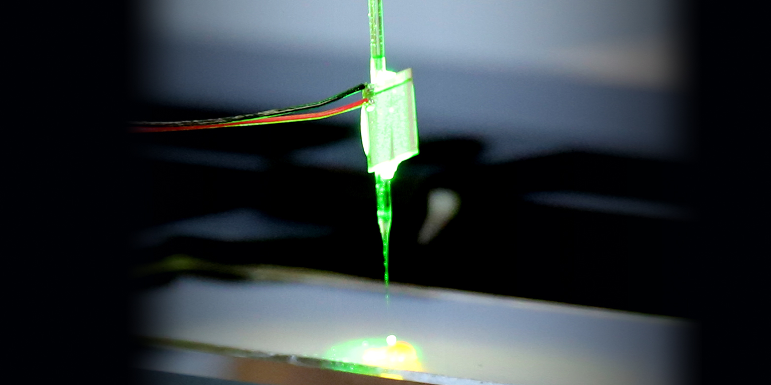 The glass needle that captures the particles glows neon green. 