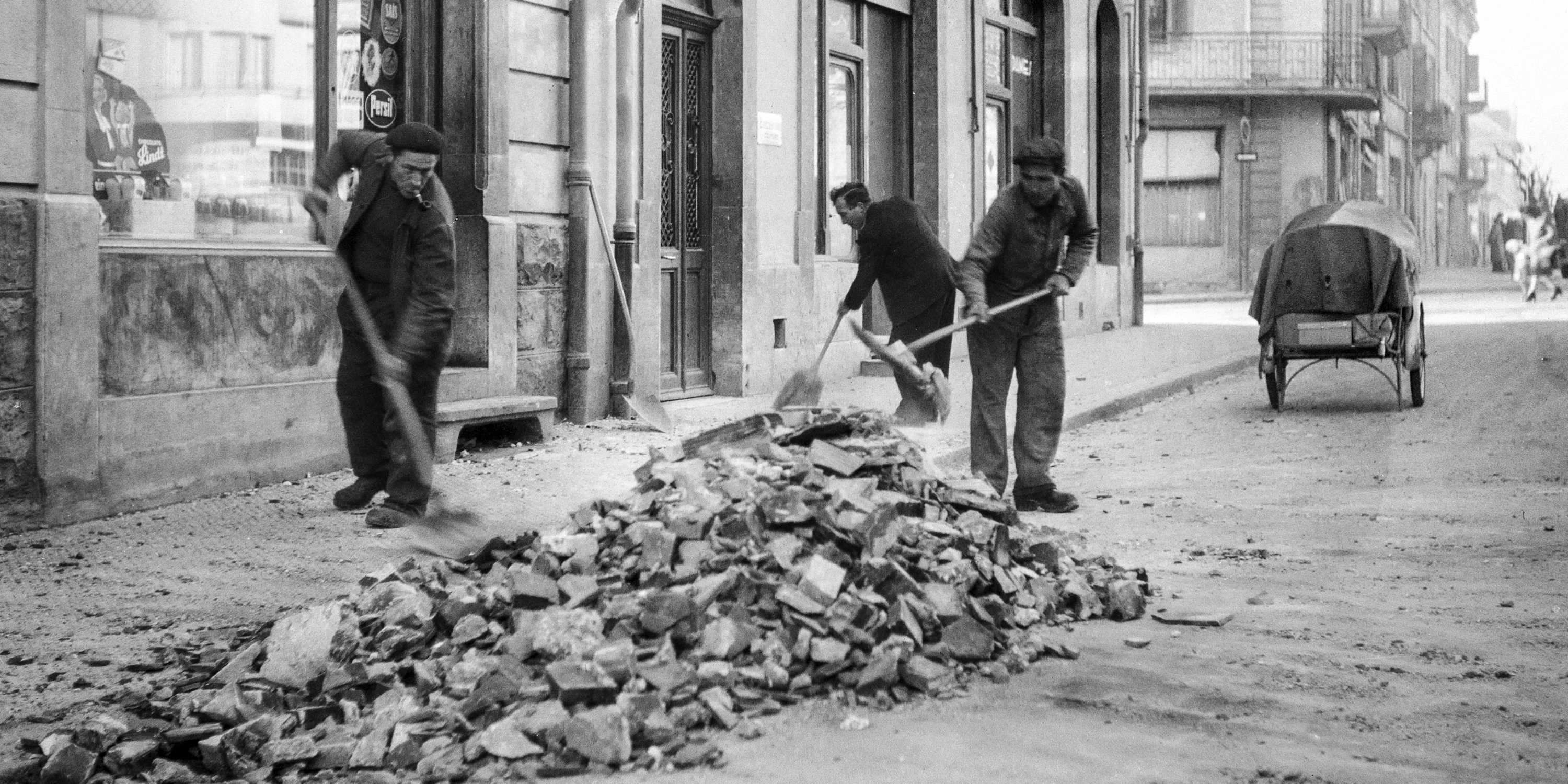 Old black and white picture of three men sweeping debris from the street.