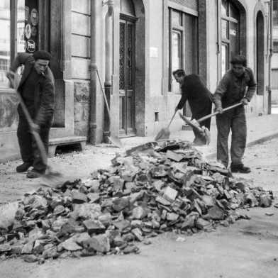 Old black and white picture of three men sweeping debris from the street.