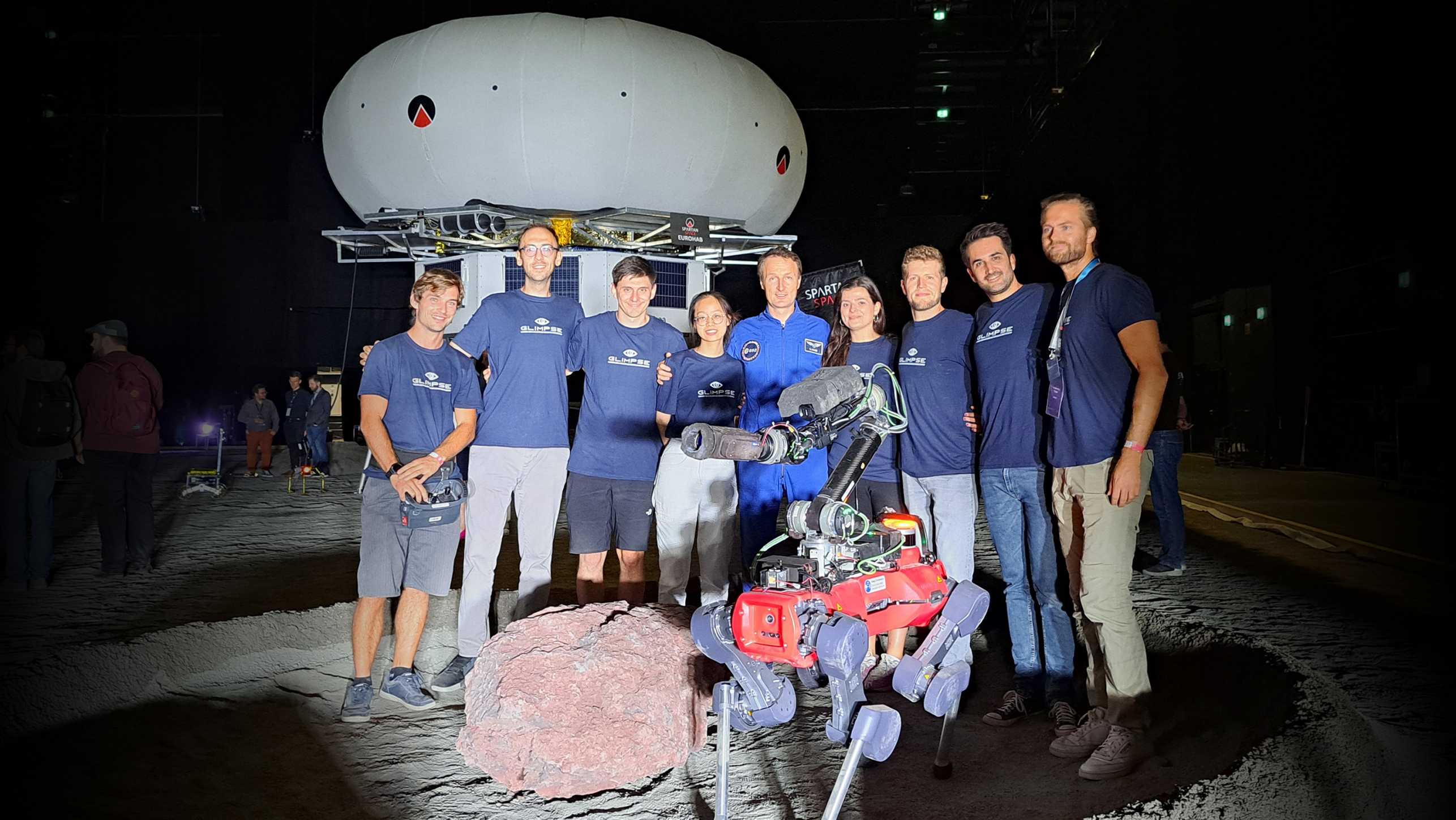 Group photo of the team at night in a gravel pit, with their legged robot in front of them.