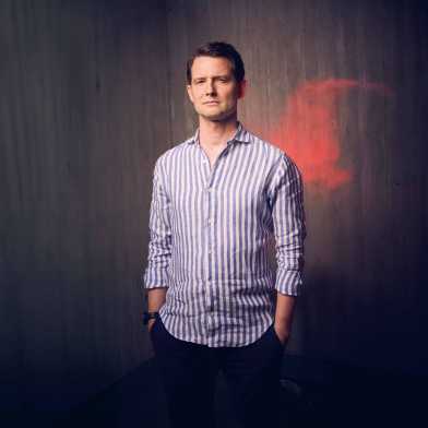 Fabian Unteregger in front of a wooden wall, behind him a cloud of red smoke
