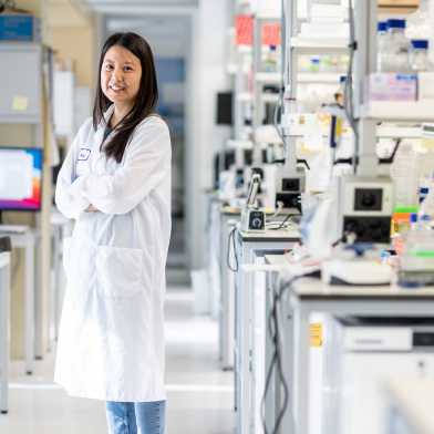 Woman standing in the laboratory with her arms crossed. She is wearing a lab coat.