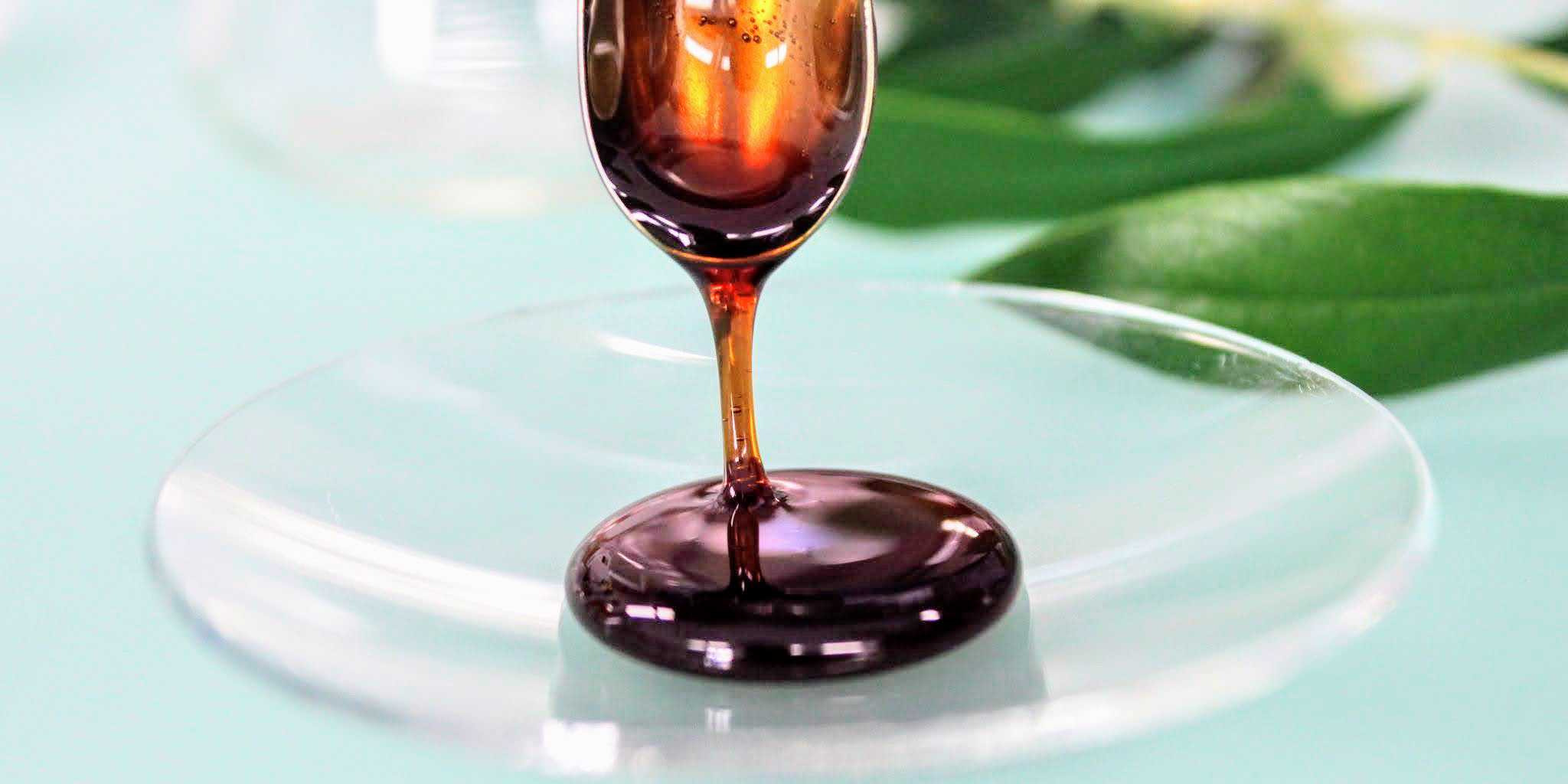 Substance that looks like dark honey runs from spoon to glass bowl. 