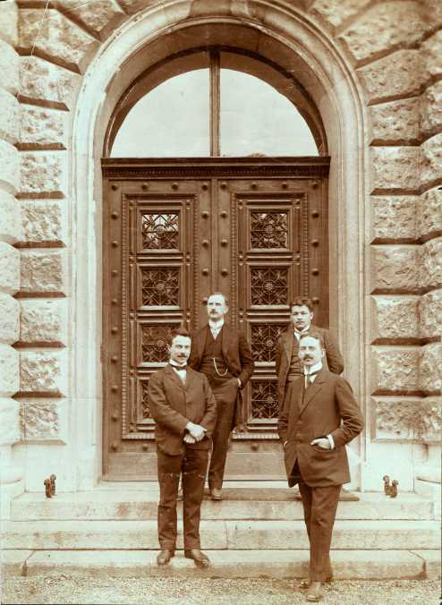 Enlarged view: Old picture on which four people are standing in front of the wooden door.