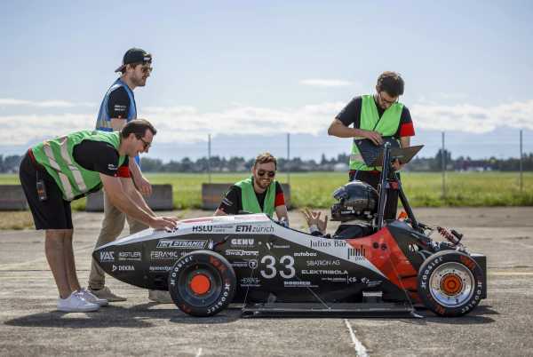 Four men stand around the crewed electric race car, beaming all over their faces.
