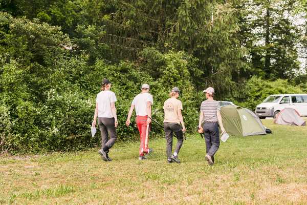 The four students walk across a meadow to their tents.