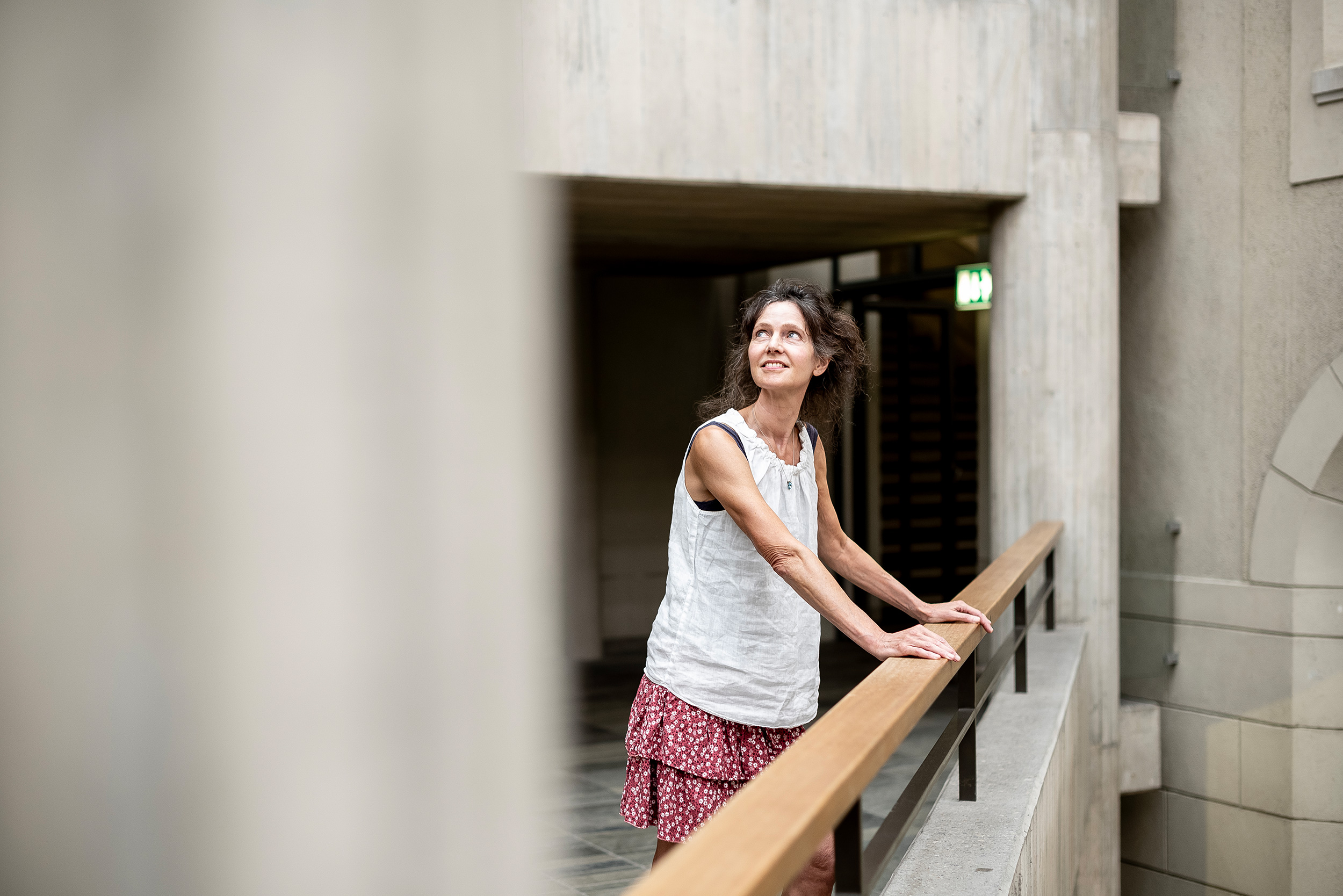 Sara van der Geer in the ETH Zentrum building, leaning on the railing and looking up at the ceiling with a smile.