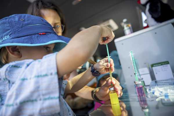 Child draws up syringe with the help of the mother.