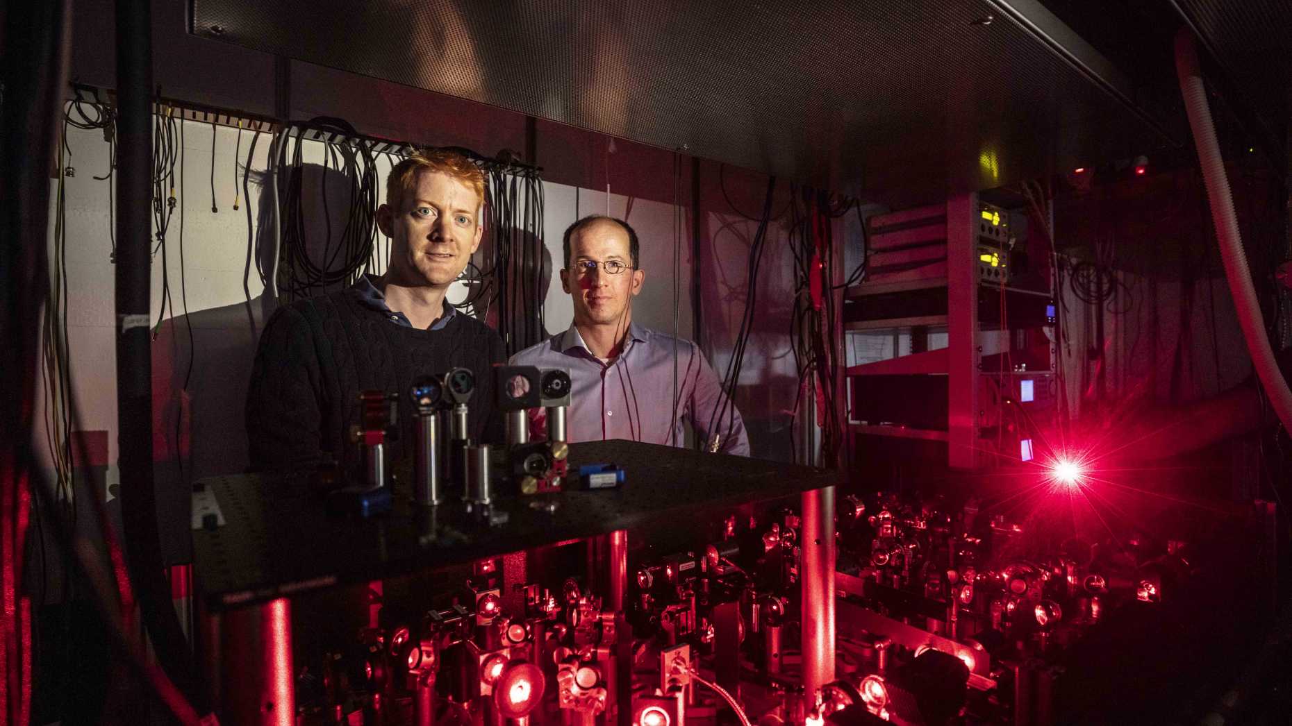 Two men stand behind Qubits. The image is dominated by red light. 
