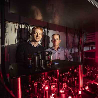 Two men stand behind Qubits. The image is dominated by red light. 