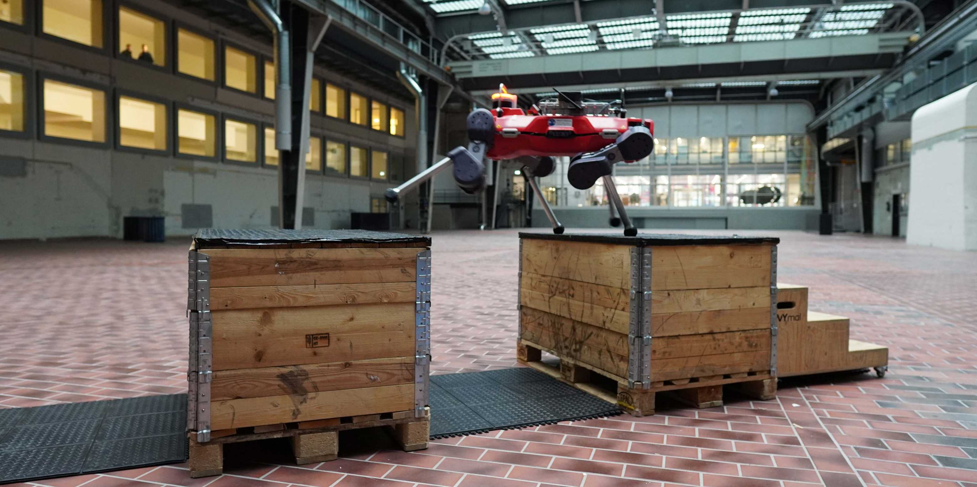 The four-legged robot steps over a gap between two wooden boxes.