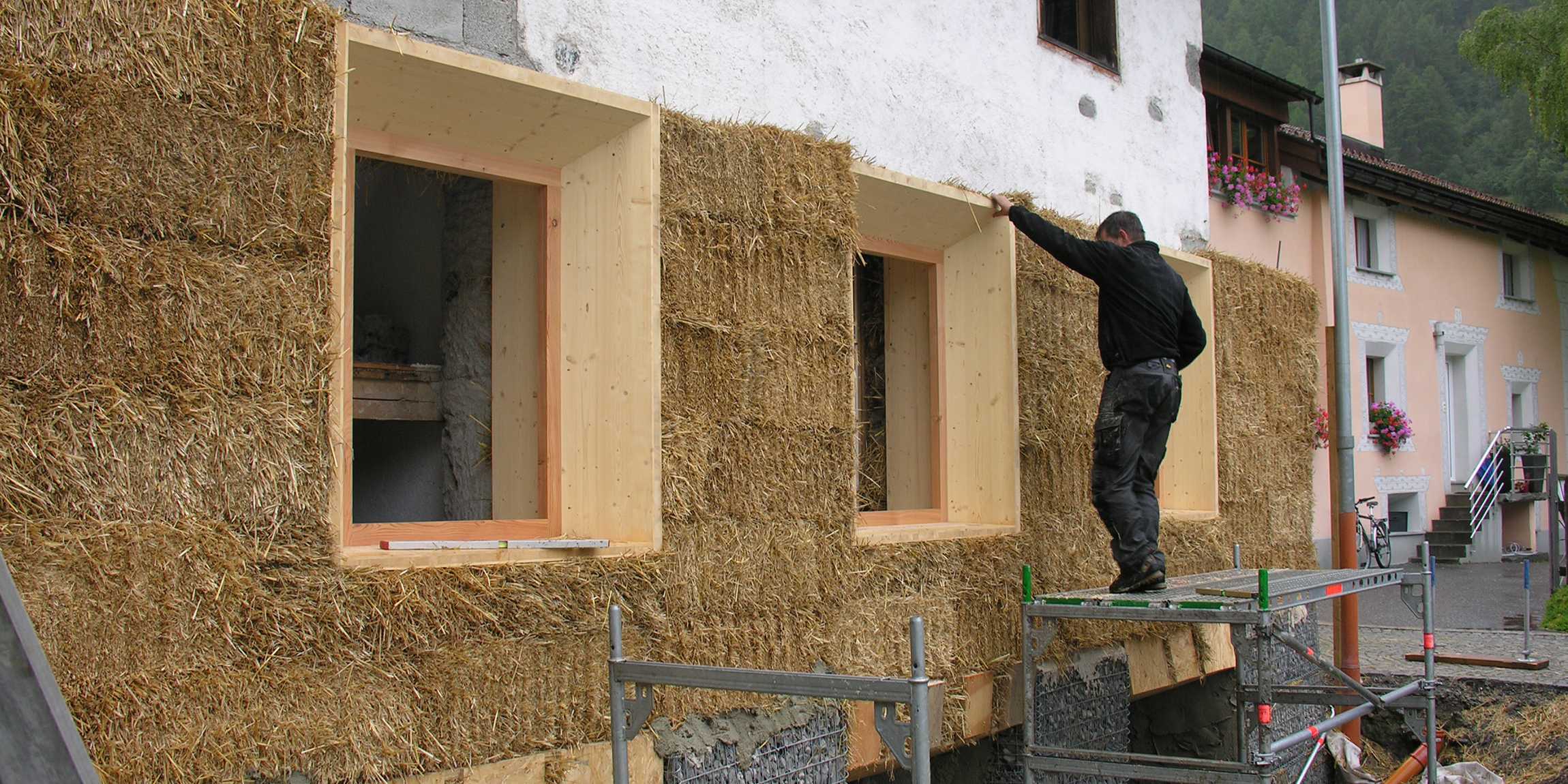 A man works on a house facade with straw.