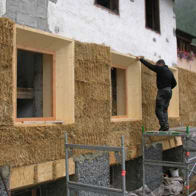 A man works on a house facade with straw.