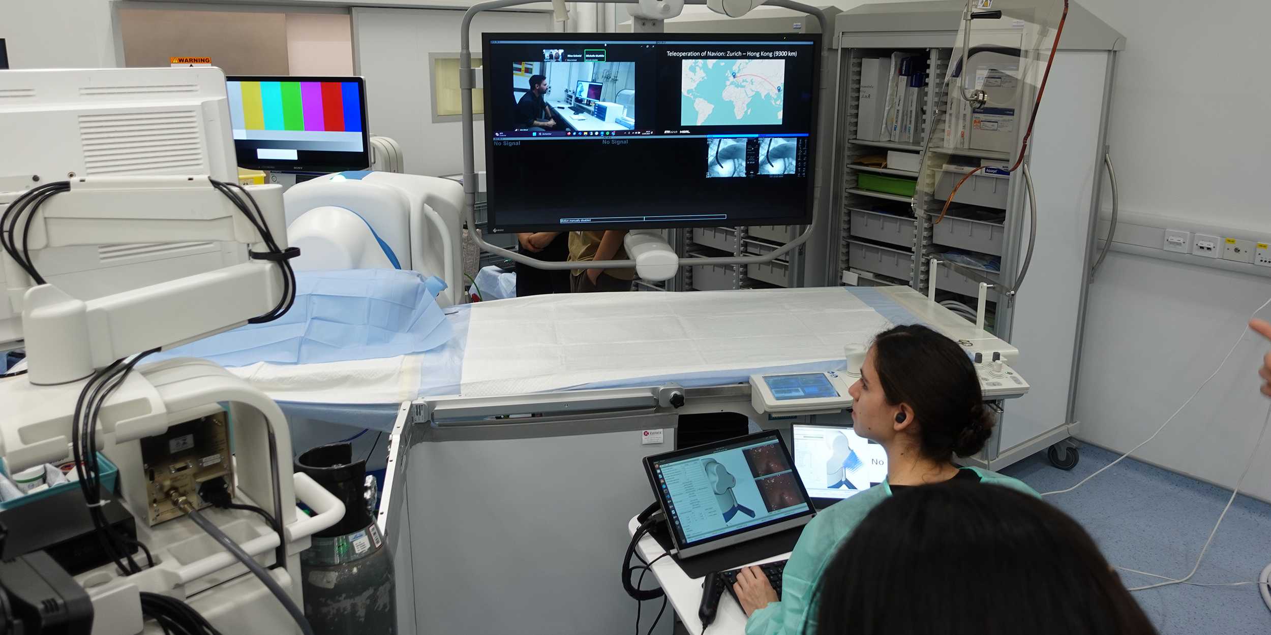 A surgeon in the operating theater is sitting in front of a screen showing the live feed from Zurich.