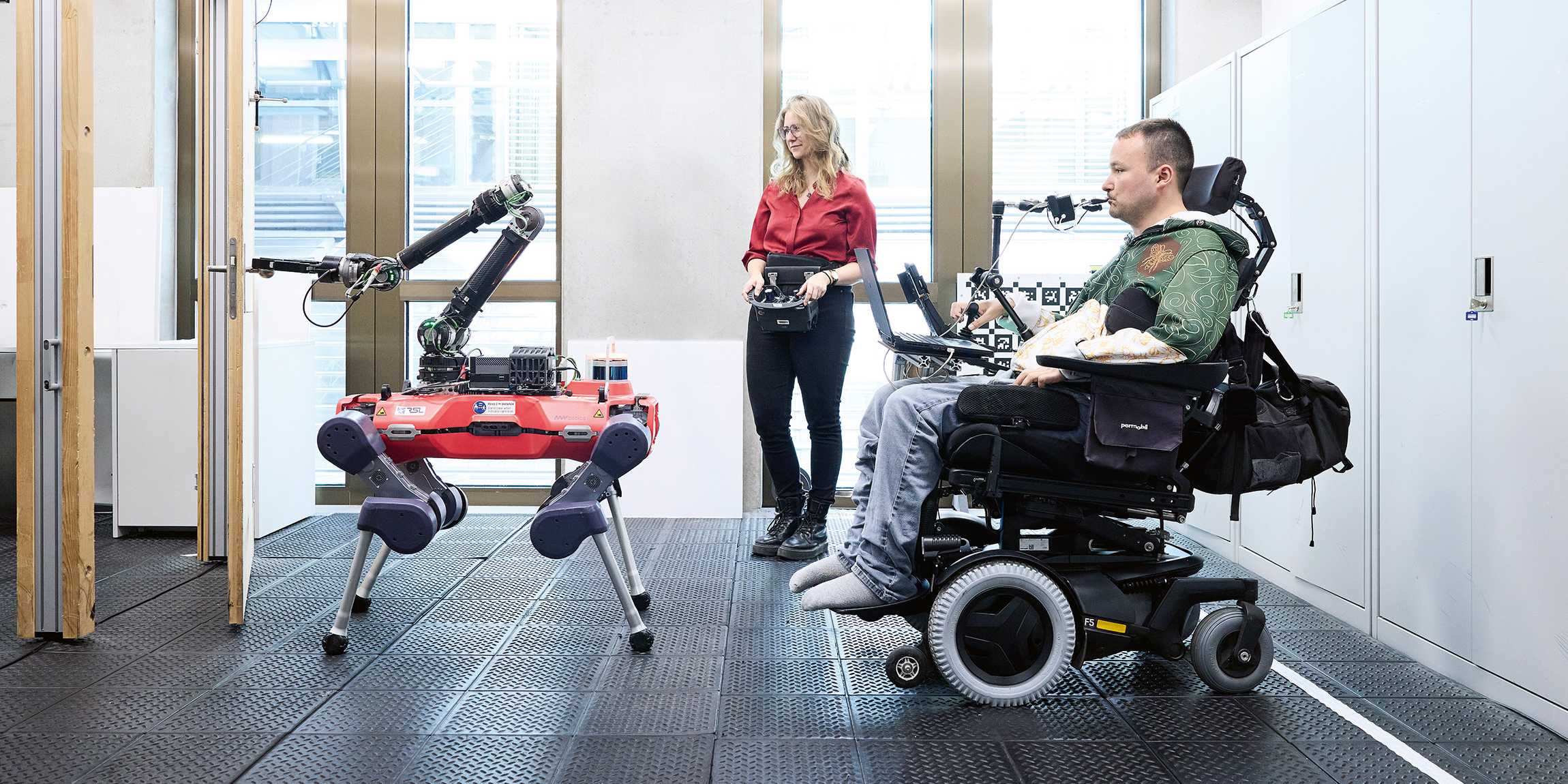 A four-legged robot holds the door open for a man in a wheelchair.