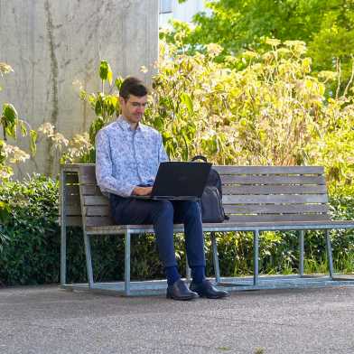 Kiril Vasilev sits on a bench and works on his laptop