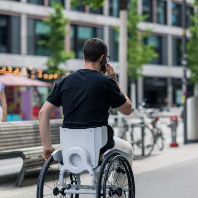 Someone in a wheelchair gives one hand, the other he has on the phone.