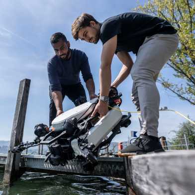 Two people place a robot in the water