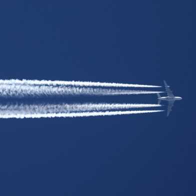 View from below of an aircraft with vapour trails